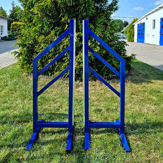 A pair of blue aluminum training wings for horse jumping, placed on grass in front of a building with a tree in the background.